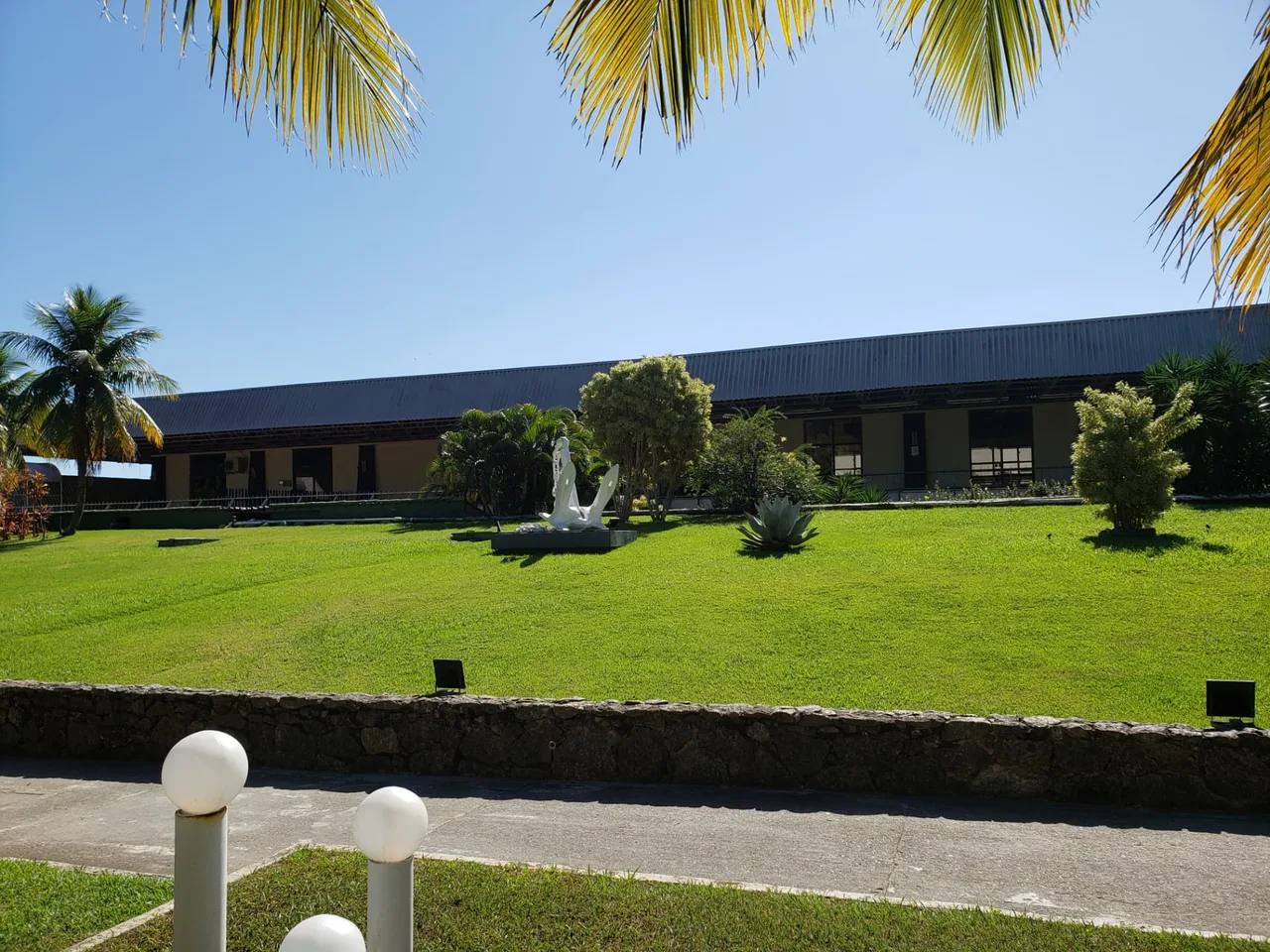 Jardins do Clube Naval Charitas com escultura de âncora e coqueiros